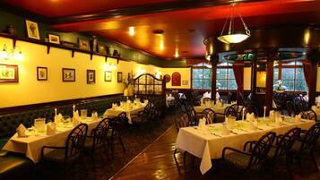 A restaurant with multiple tables set for dining, a green cushioned bench along the wall, and framed pictures on the wall.