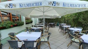 An outdoor seating area with tables and chairs under a large umbrella with 'KULMBACHER' branding. - Jembo Park (Jena)