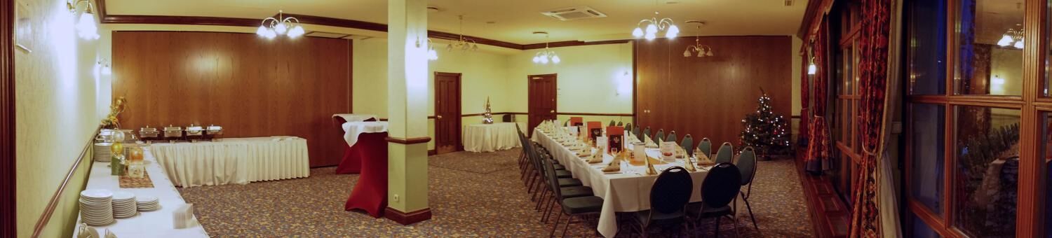 A banquet hall with a long table set for a meal, a Christmas tree, and a stage with a podium.