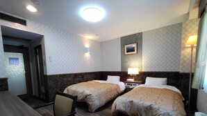 Habitación de hotel con dos camas, un escritorio y una silla. Se observa un cuadro en la pared y una lámpara en el escritorio.