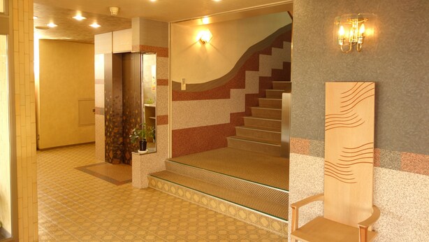 Vestíbulo de hotel con una escalera, mostrador de recepción y una lámpara fijada a la pared.