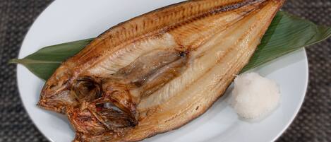 A white plate with a whole fried fish, a leaf, and a mound of rice.