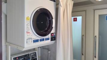 Una lavandería compacta y moderna con lavadora y secadora de carga frontal, panel de control y una tubería de agua visible.