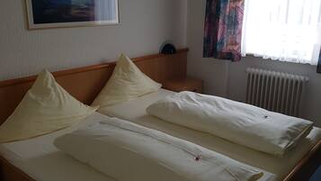 Habitación de hotel con una cama grande, cabecero, un cuadro en la pared, ventana con cortinas y un radiador.
