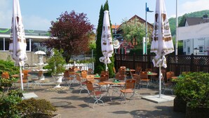 An outdoor patio with tables and chairs, umbrellas, and a fountain. - Hotel Stadt Baunatal (Baunatal)