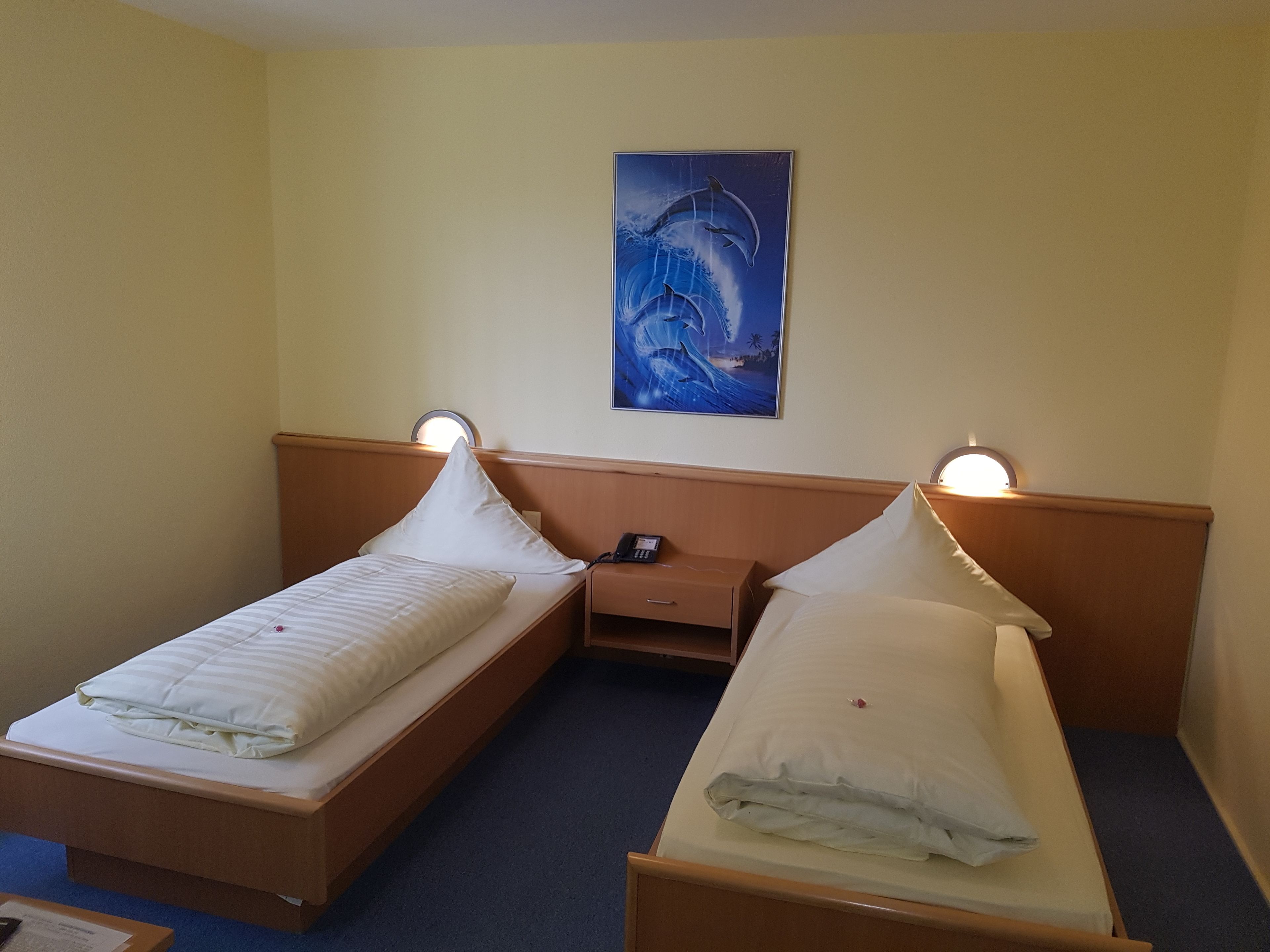 A hotel room with two single beds, a nightstand, a wall-mounted painting, and bedside lamps.
