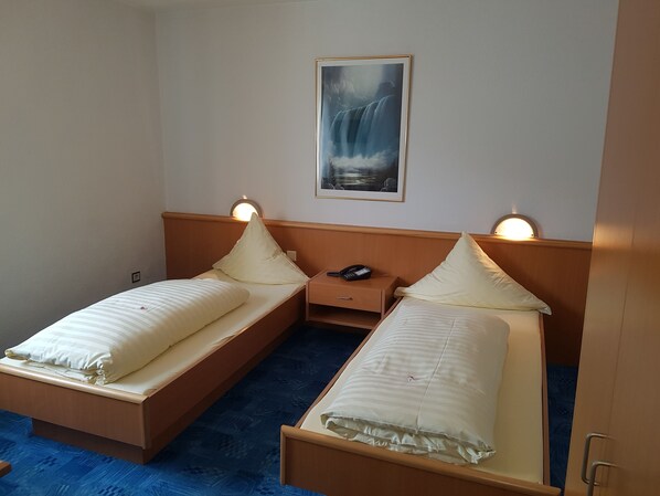 A hotel room with two single beds, a nightstand with a phone, and a painting of a waterfall on the wall.