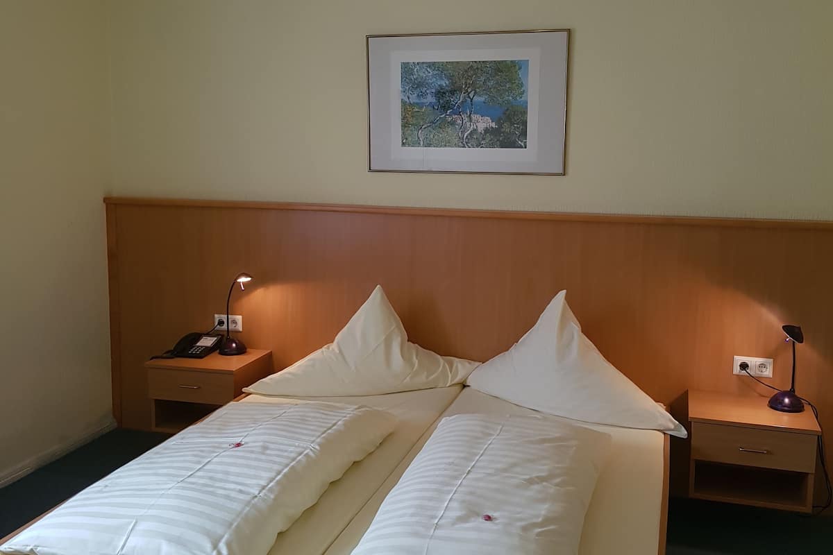A hotel room with a wooden bed, two bedside tables with lamps, a framed picture on the wall, and a ceiling light.