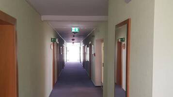 Un largo pasillo de hotel, estrecho, con puertas a ambos lados, suelo alfombrado y letreros de salida de emergencia.