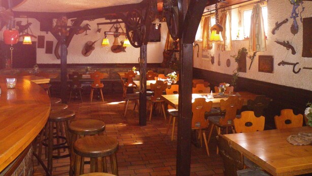 A restaurant interior with brick flooring, wooden tables and chairs, hanging lights, and wall-mounted decorations. - Hotel Stadt Baunatal (Baunatal)