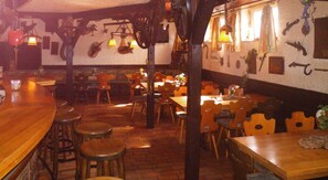 A restaurant interior with brick flooring, wooden tables and chairs, hanging lights, and wall-mounted decorations. - Hotel Stadt Baunatal (Baunatal)
