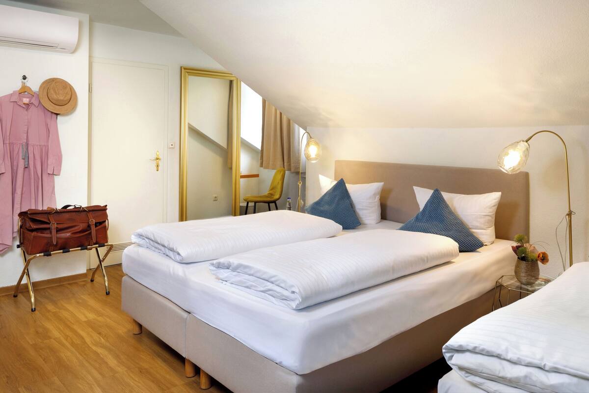 A hotel room with two beds, a mirror, a hat, and a suitcase.