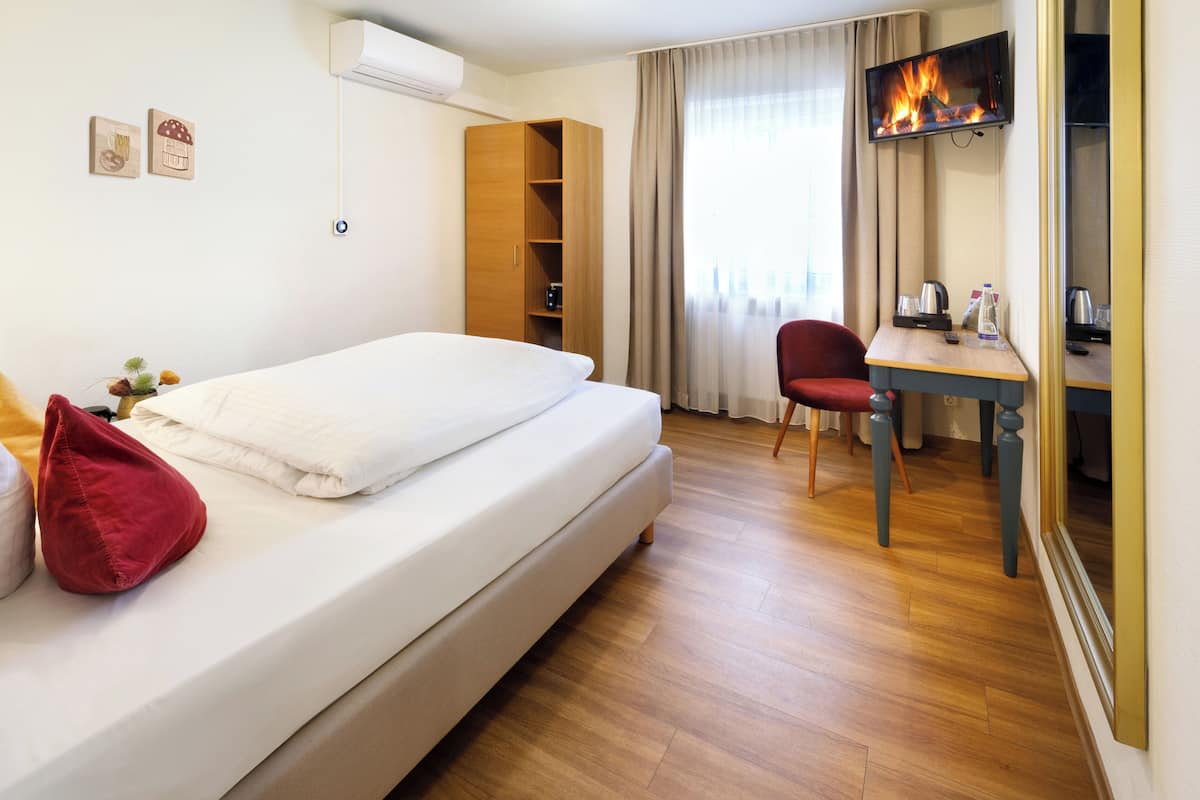 A hotel room with a bed, a desk, a chair, a TV, and a wardrobe.