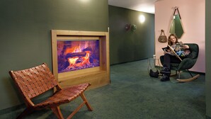 A room with a wooden chair, a fireplace with a fire, a green sofa, and a wall clock. - Rosi Boutique Hotel (Regensburg)