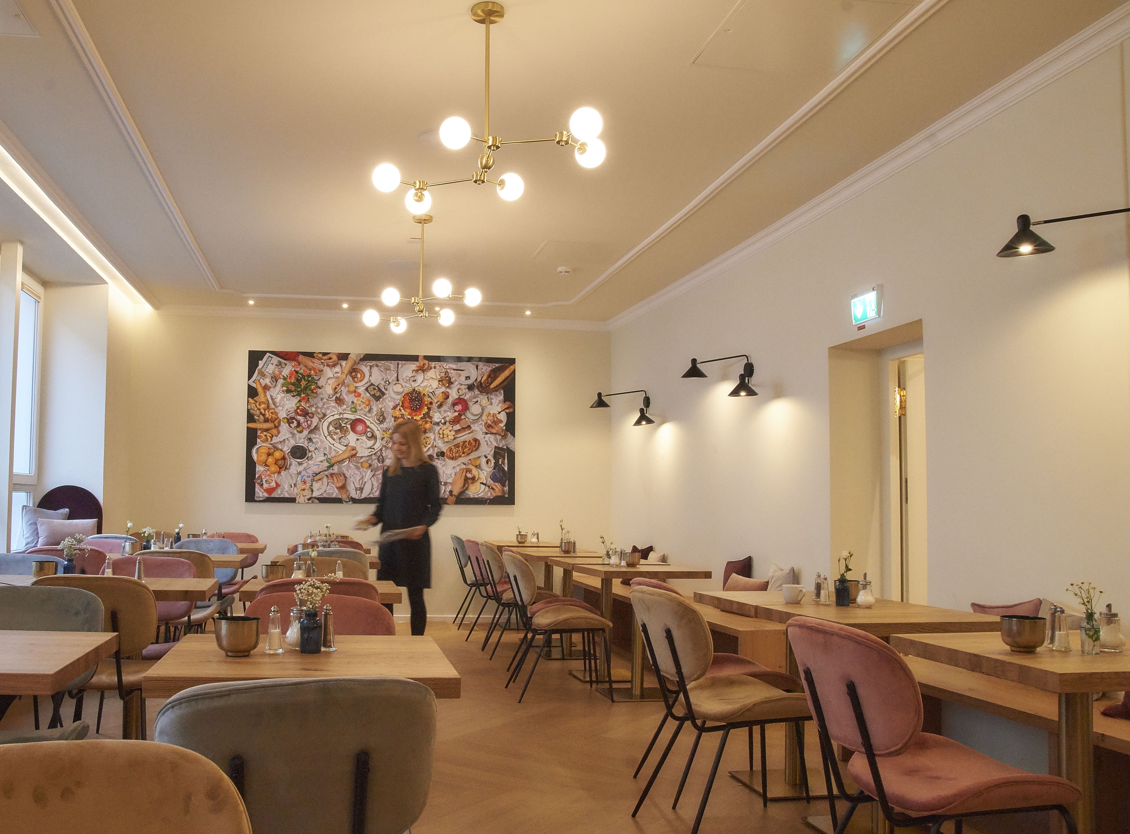 Interior de restaurante con varias mesas y sillas, un gran cuadro decorativo en la pared y una lámpara en el techo.