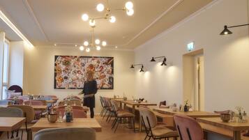 Interior de restaurante con varias mesas y sillas, un gran cuadro decorativo en la pared y una lámpara en el techo.