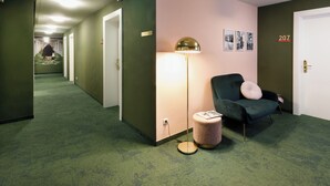 A hallway with green carpet, a green armchair with a pink cushion, a floor lamp, and a door labeled 207. - Rosi Boutique Hotel (Regensburg)