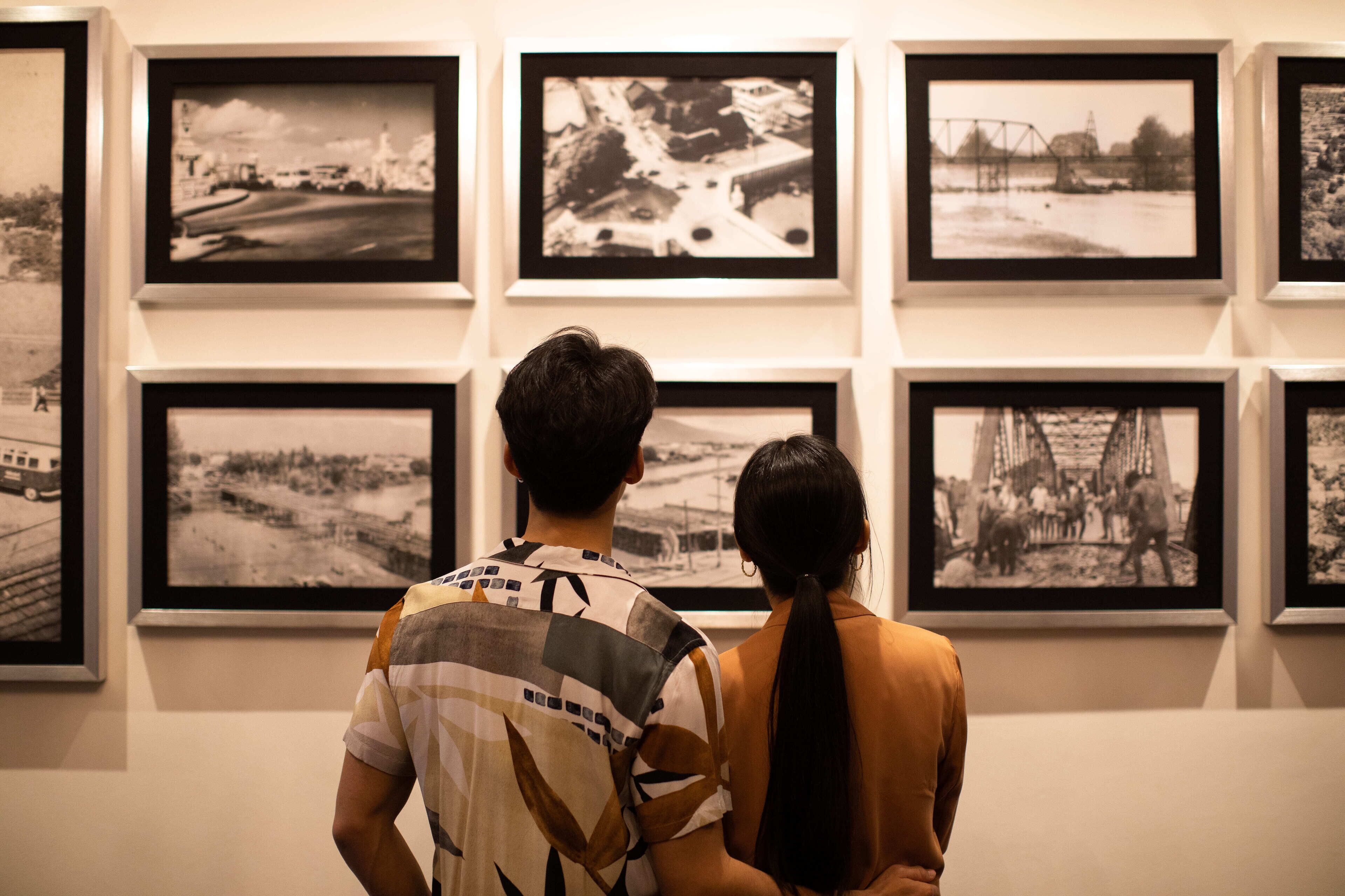 Um casal observando fotografias preto e branco em uma parede.