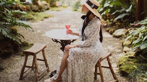 A woman sitting at a wooden table in a lush garden with ferns and greenery. - The Bridge An Eclectic Luxotel Chiangmai (Chiang Mai)