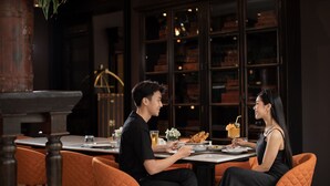 A couple dining at a table with a view of a bookshelf and a staircase in the background. - The Bridge An Eclectic Luxotel Chiangmai (Chiang Mai)