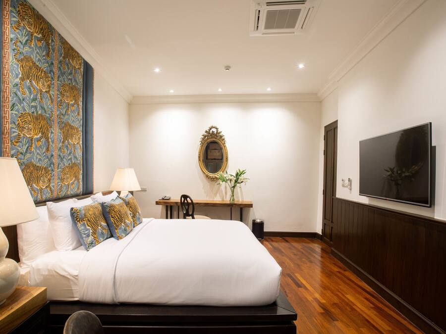 Ein Hotelzimmer mit einem großen Bett, zwei Nachttischlampen, einem Flachbildfernseher, einem Holzboden und einem Wandteppich als Dekoration.