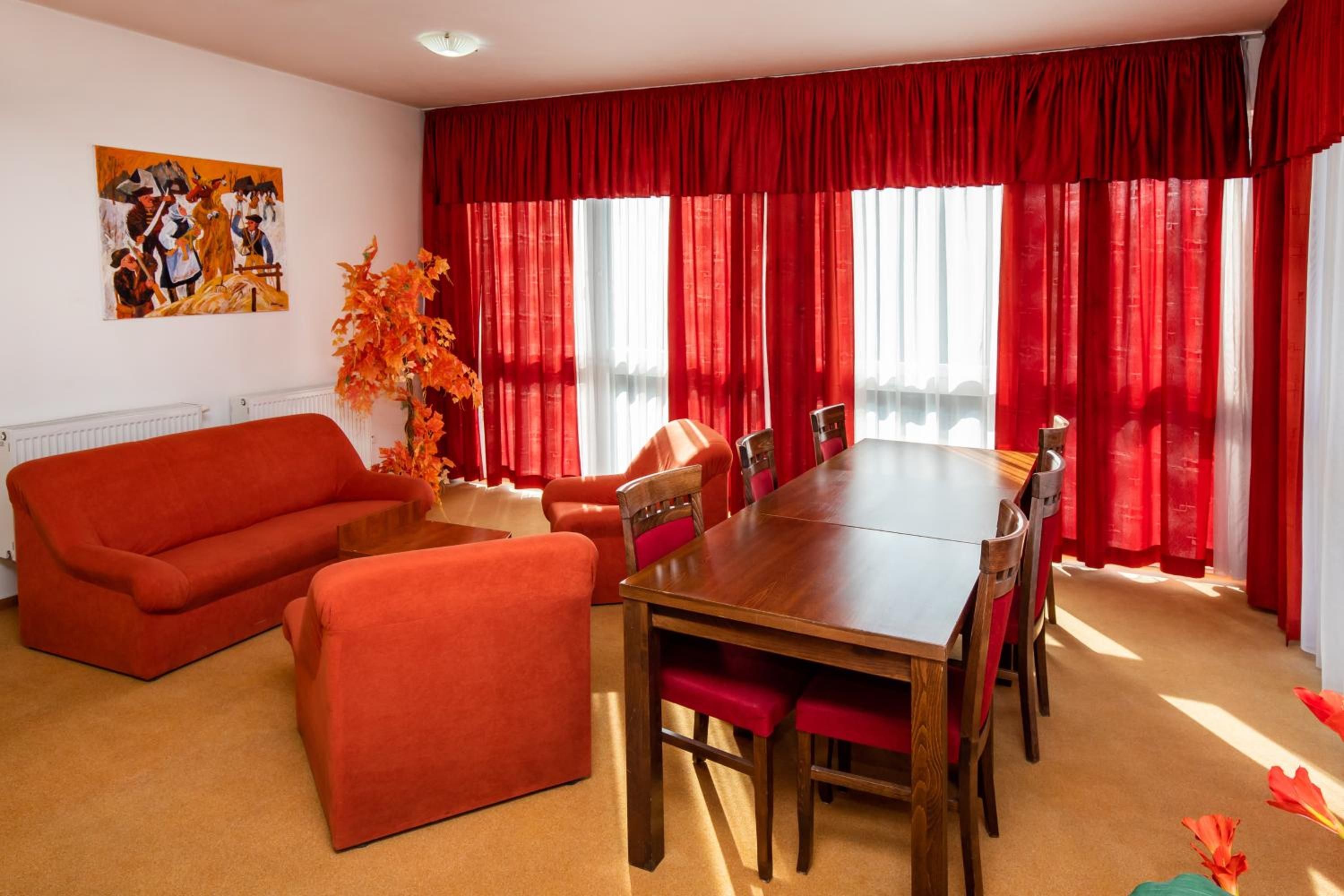 A room with a red sofa, a wooden dining table with chairs, and a large window with red curtains.