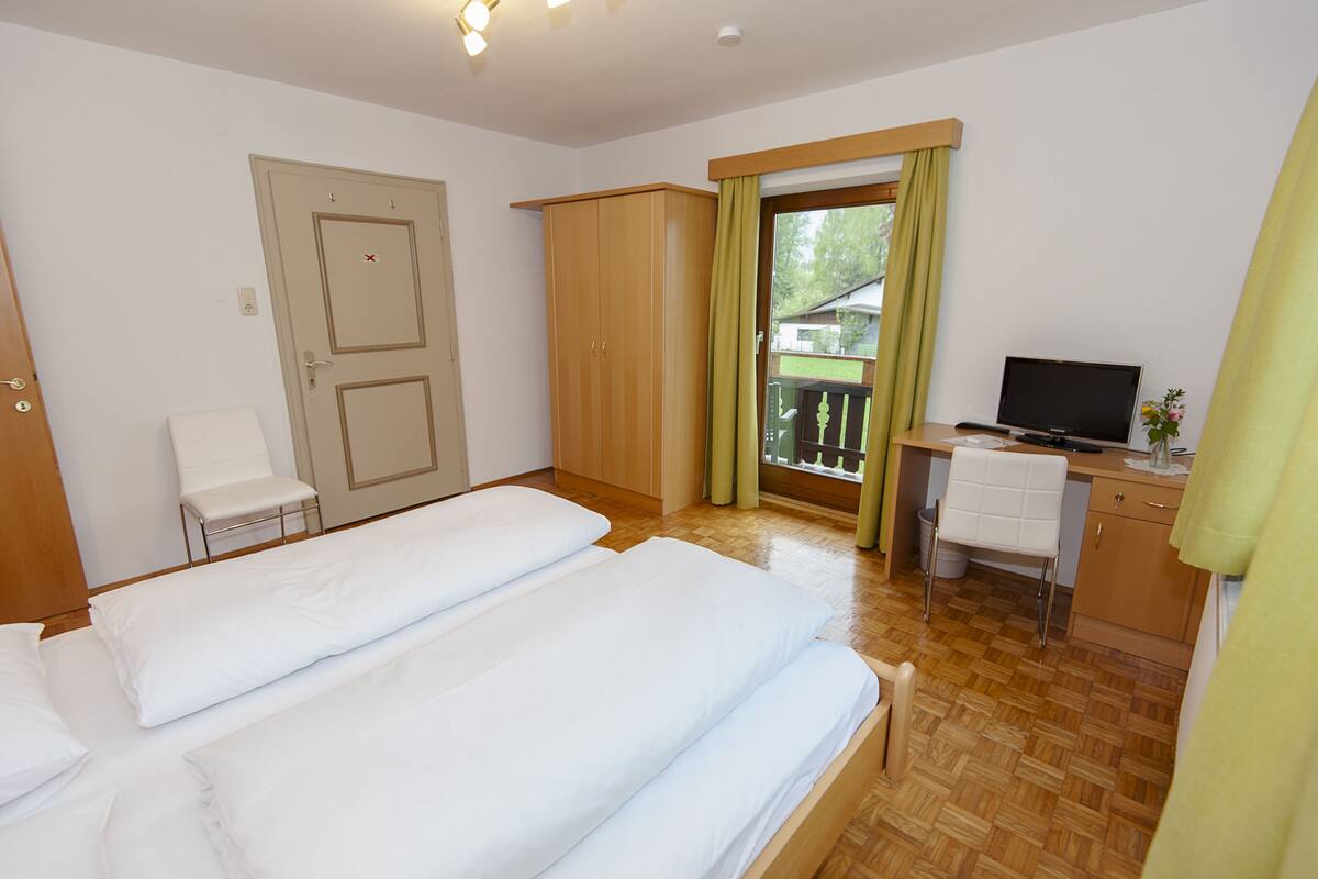 A hotel room with two beds, a desk with a TV, a chair, and a wardrobe.