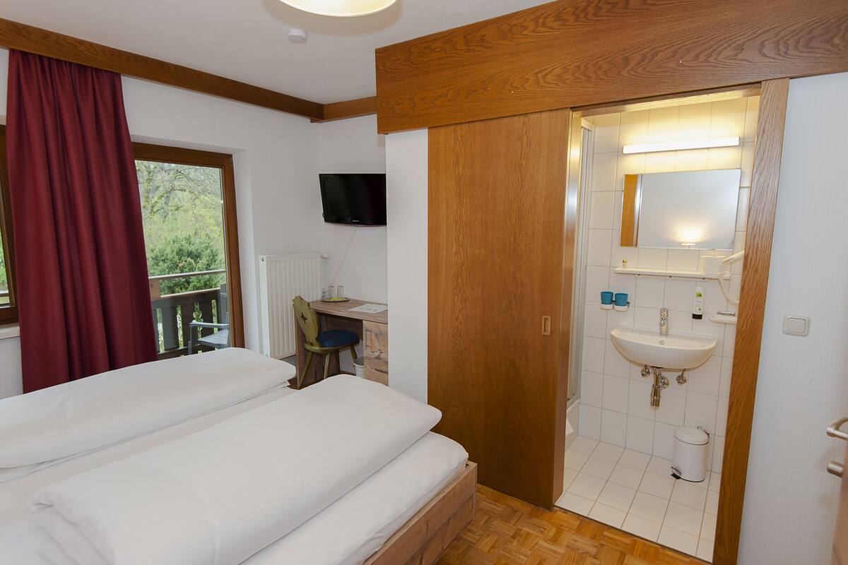 A bedroom with two beds, a wooden door, a bathroom with a sink, and a TV mounted on the wall.