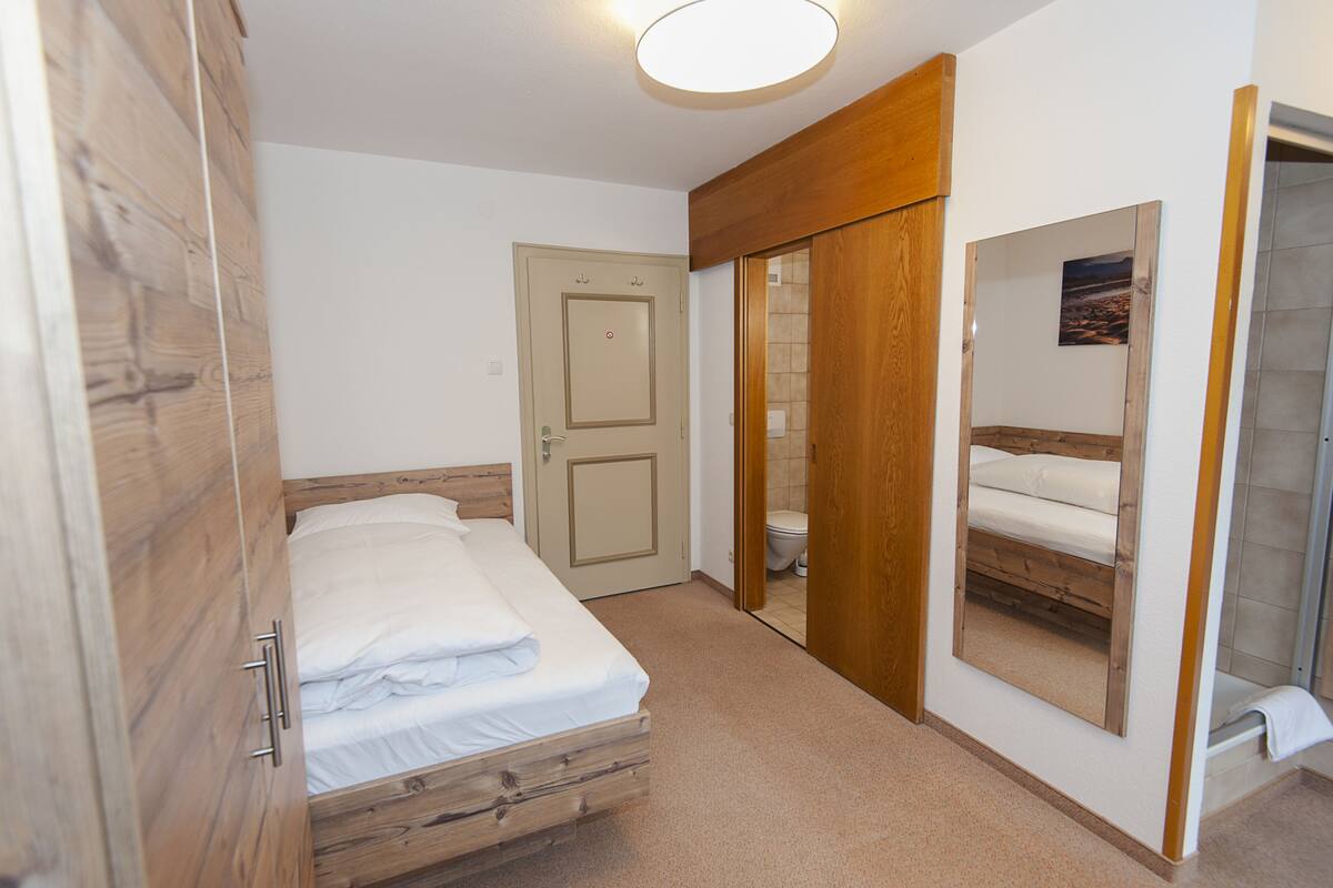 A bedroom with a wooden bed, a wardrobe, a door, a mirror, and a shower area.