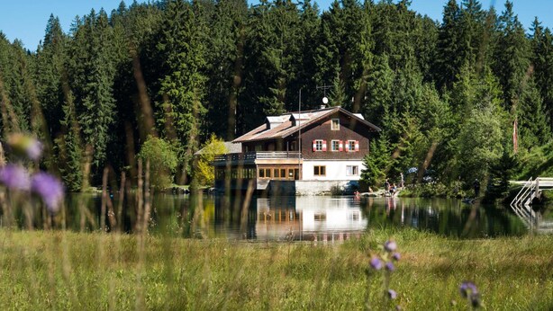 A house by a lake with a wooden deck and a small dock. - Pension Leuprecht (Lechaschau)