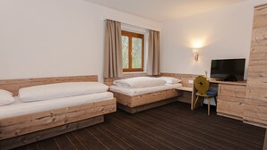 A room with two wooden beds, a small desk with a chair, a television, and a window with curtains. - Pension Leuprecht (Lechaschau)