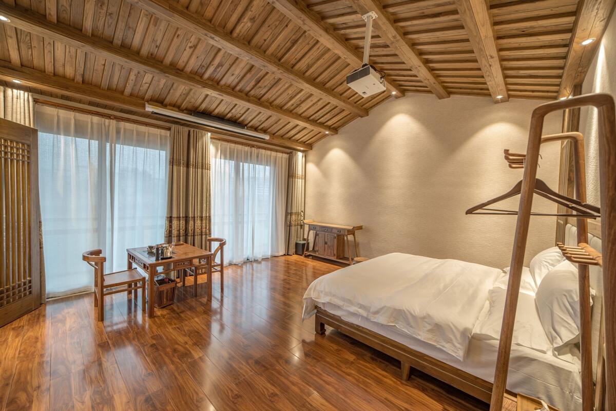 A room with a wooden ceiling, a bed, a table with chairs, and a hanging rack.