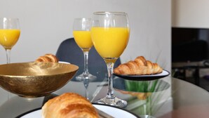 A breakfast setting with croissants, orange juice, and a brass bowl on a glass table. - Granville Apartments (Harrogate)