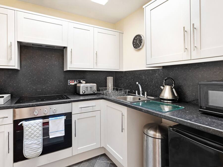 A modern kitchen with white cabinets, a black countertop, a stainless steel sink, a microwave, a kettle, and a toaster.