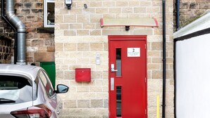 A red door with a sign indicating the number 2, a mailbox, and a car parked in front. - Granville Apartments (Harrogate)