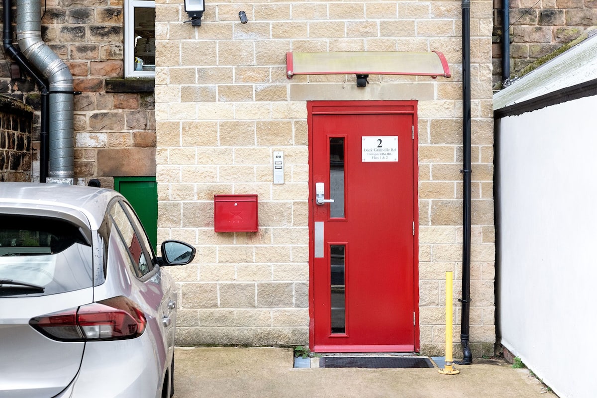 A red door with a sign indicating the number 2, a mailbox, and a car parked in front.