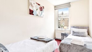 A hotel room with two beds, a window with a view of a building, and a painting on the wall. - Granville Apartments (Harrogate)
