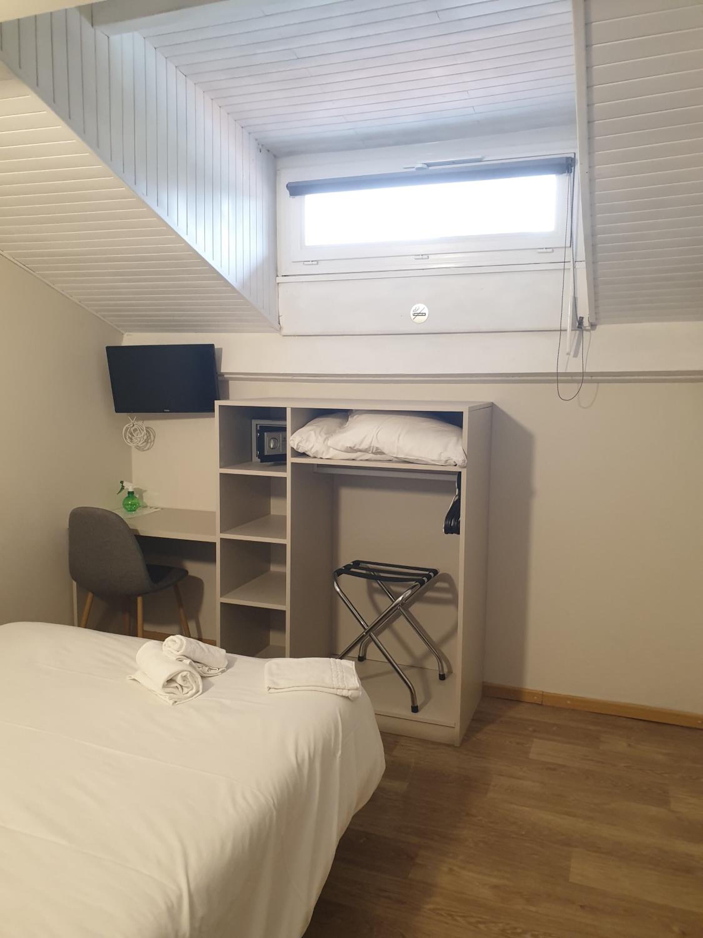 A bedroom with a loft bed, a desk, a TV, and a window.
