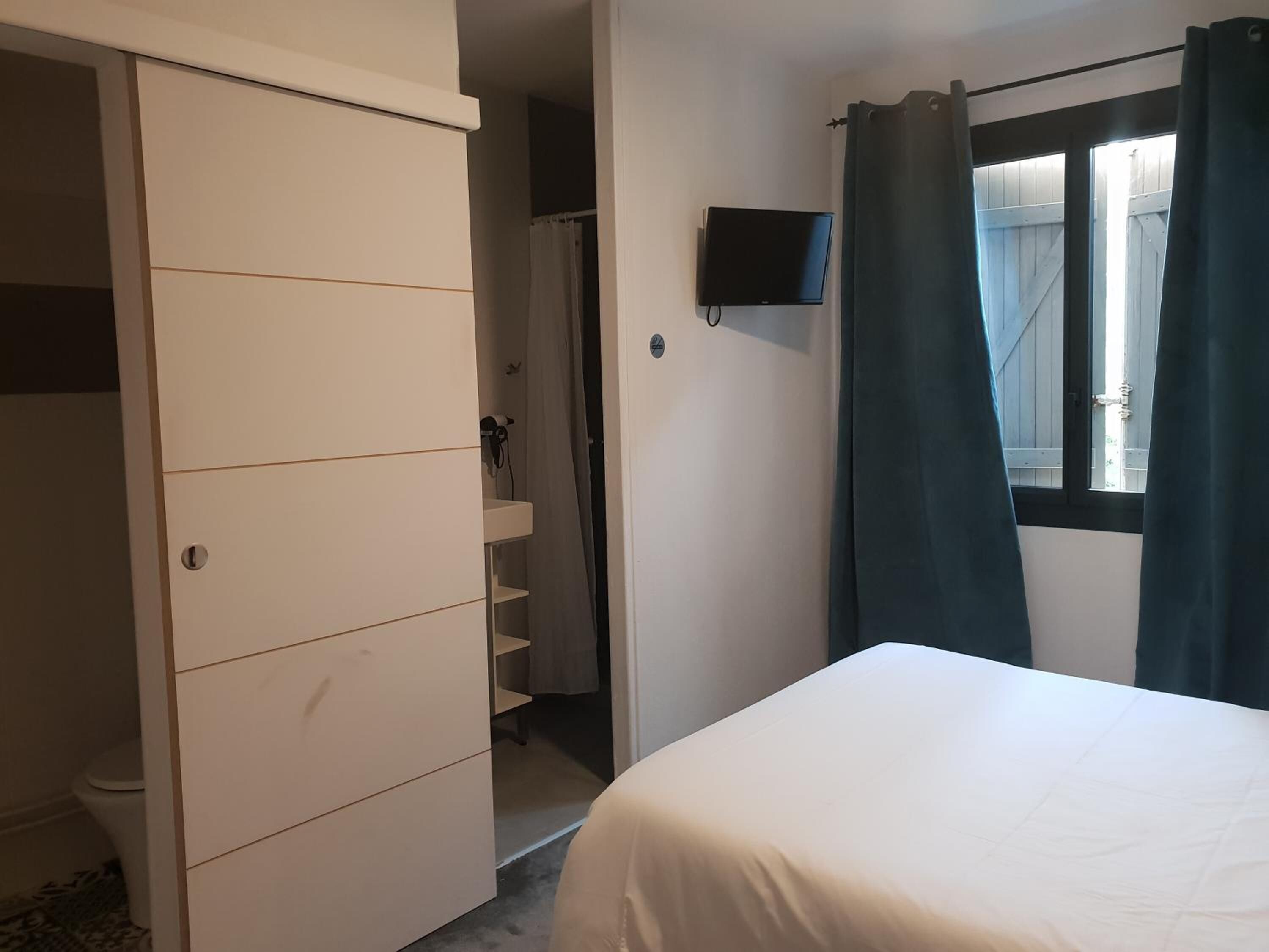 Un dormitorio con cama, armario, televisor y ventana con cortinas.