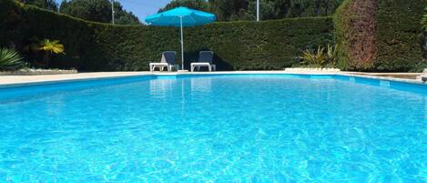 Una piscina cristallina azzurra con lettini e un ombrellone blu.