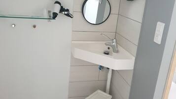 Casa de banho com lavatório branco, duas espelhas, prateleira de vidro e pavimento em azulejos estampados.