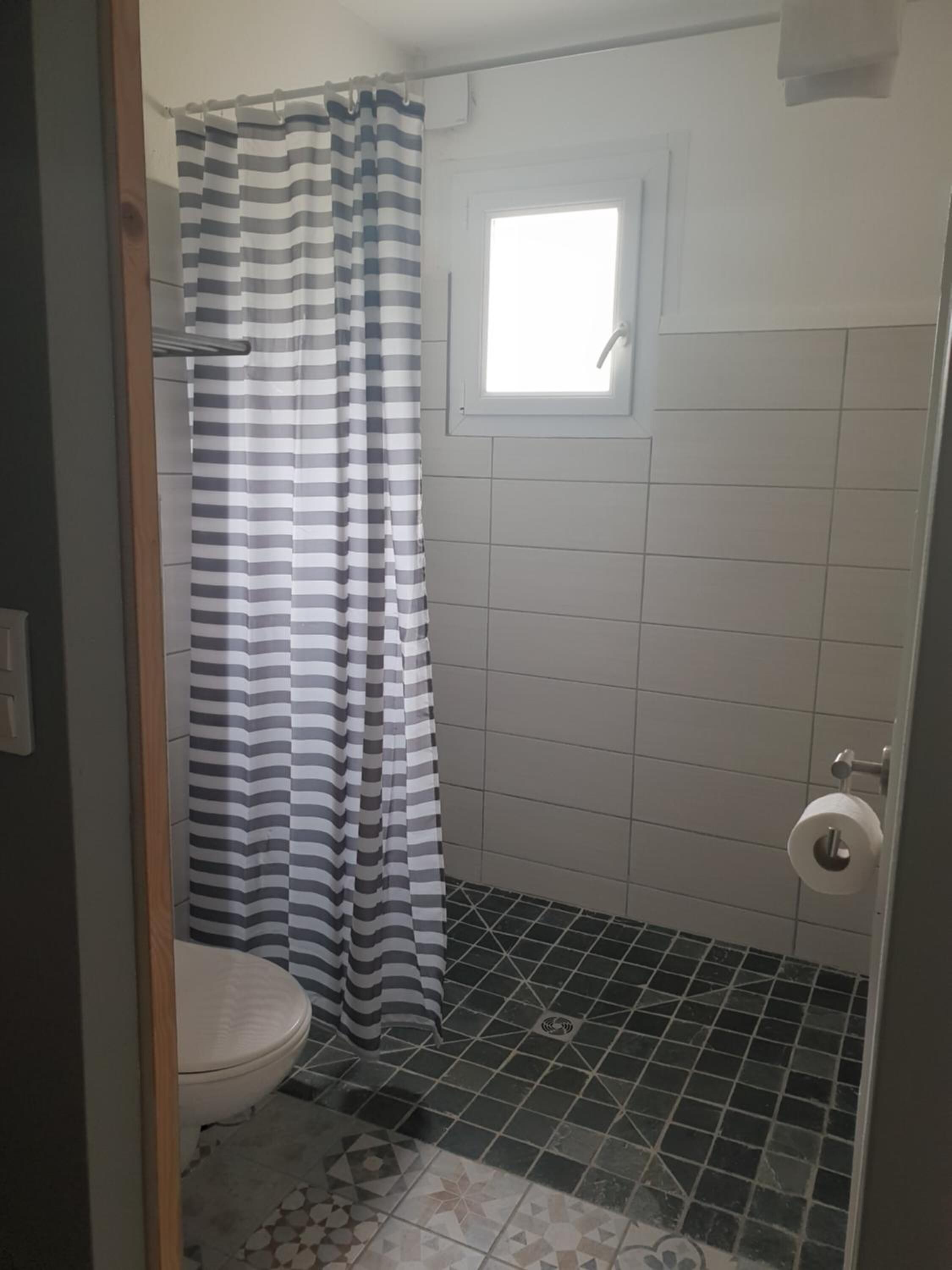 Un baño pequeño con inodoro, ducha y cortina a rayas, y ventana.