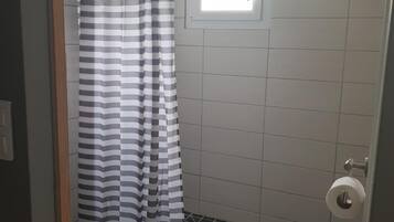 Un baño pequeño con inodoro, ducha y cortina a rayas, y ventana.