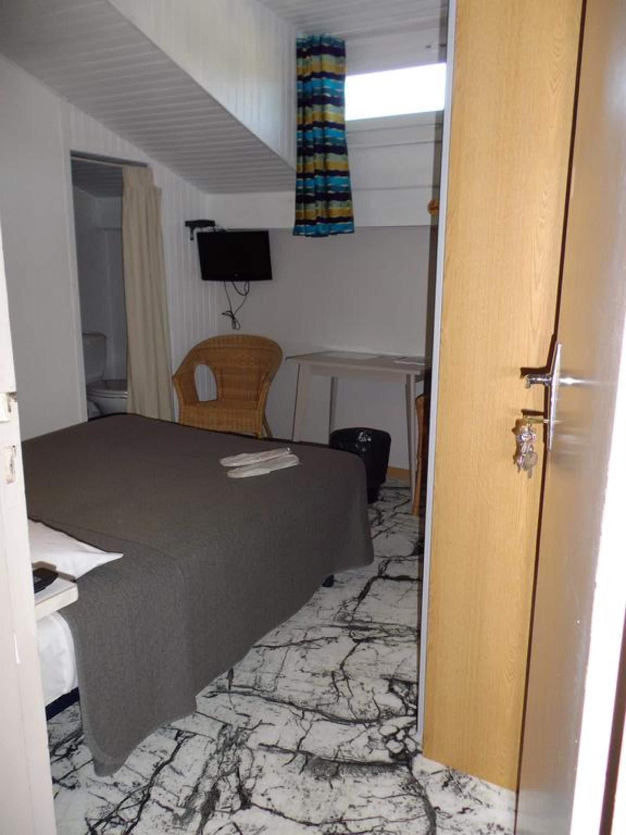 A small, single-room hotel room with a bed, a chair, a desk, and a television.