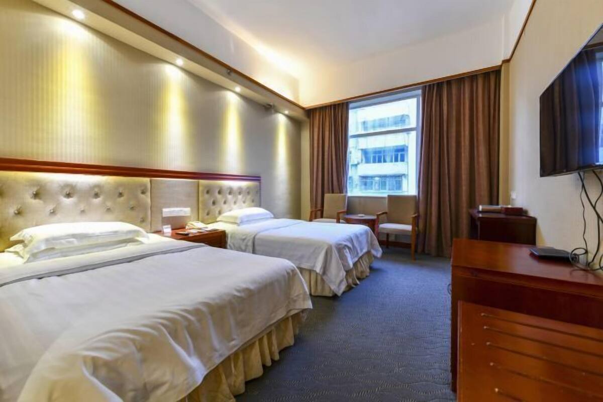A hotel room with two beds, a large window with curtains, a television, and a desk.