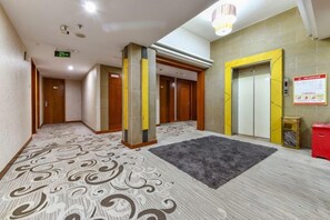 A hotel lobby with patterned carpet, wooden doors, an elevator, and a red trash bin. - Wanghailou Hotel (Huizhou)
