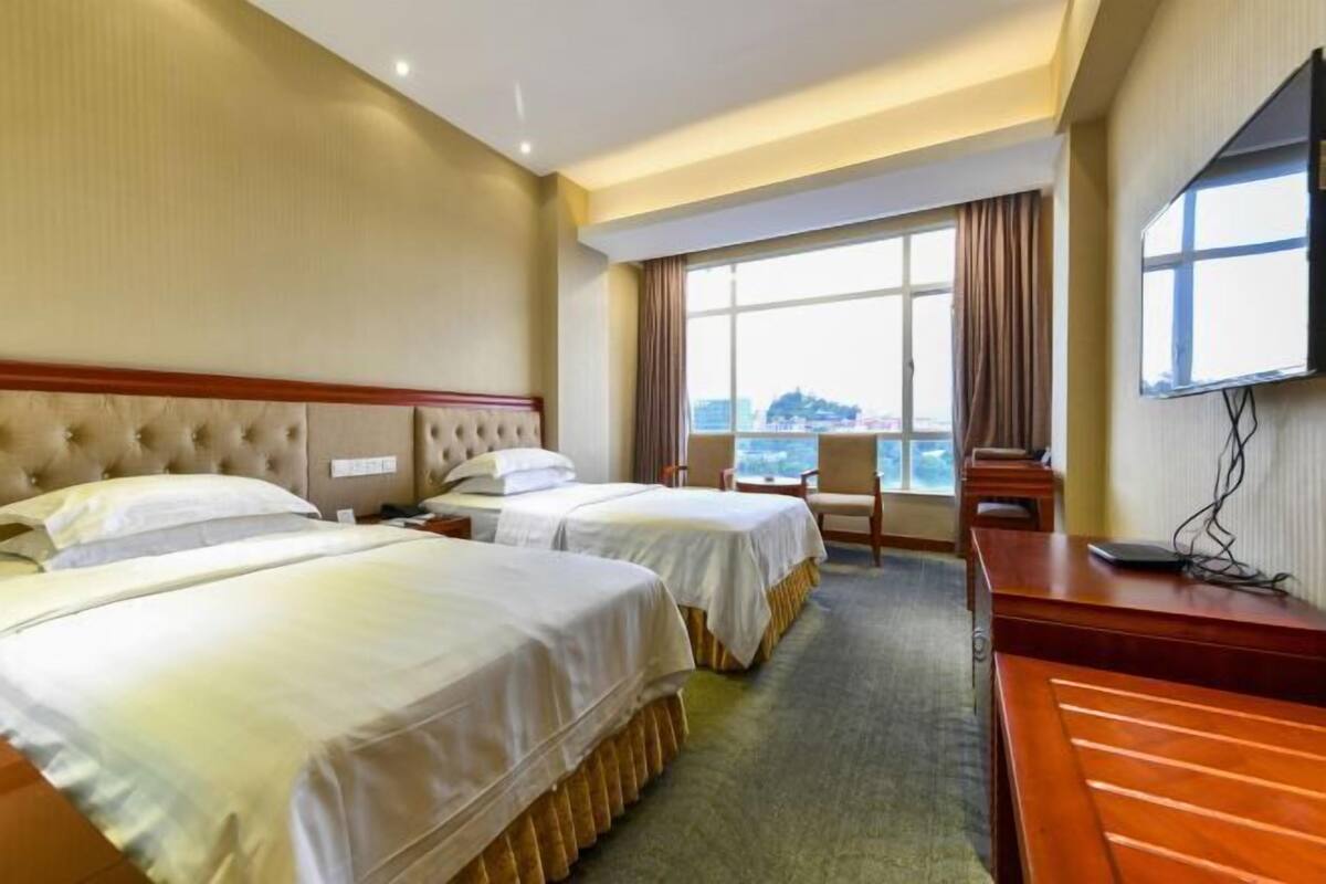 A hotel room with two beds, a desk, a chair, and a TV.