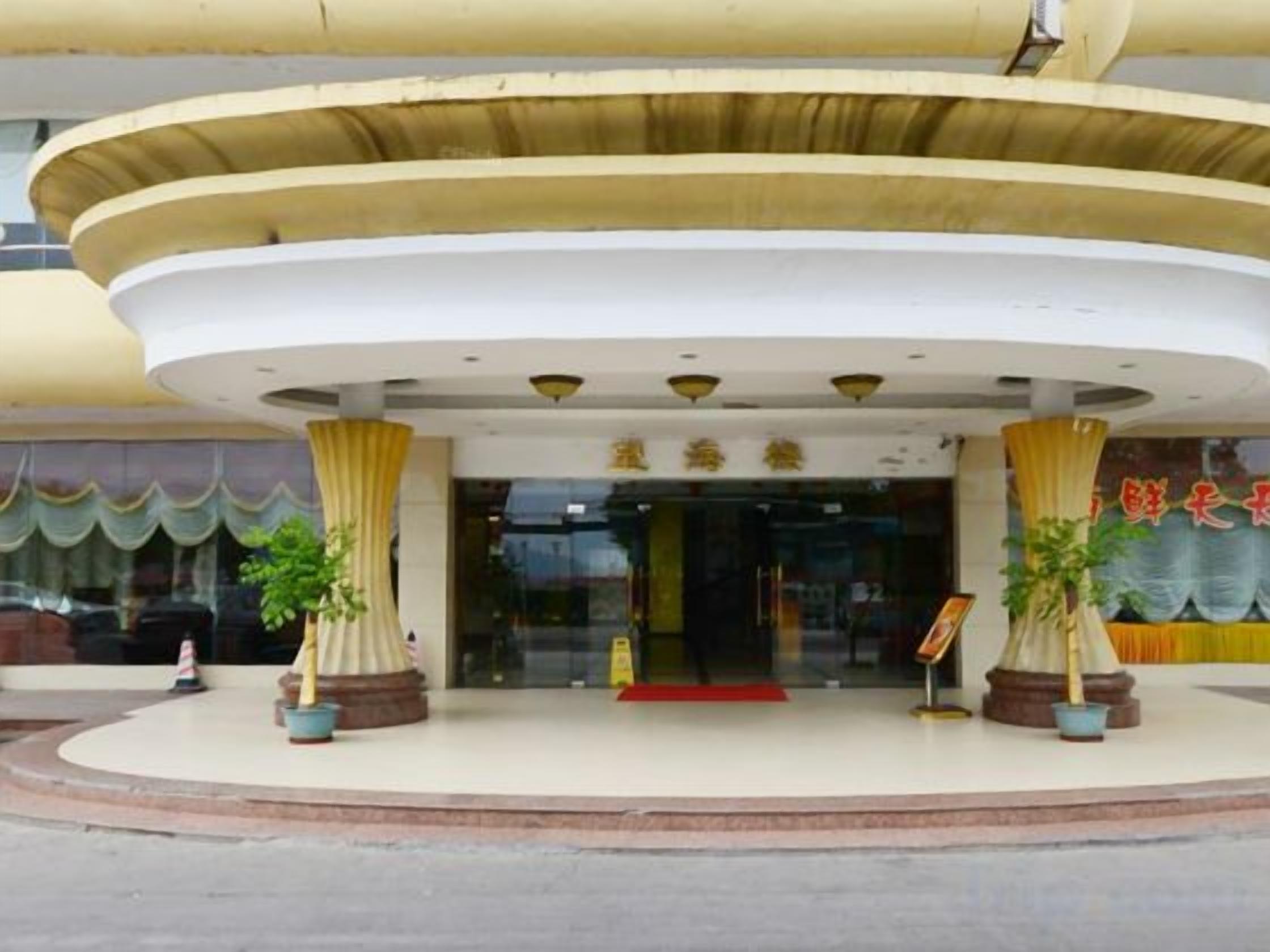 A hotel entrance with a curved facade, a red carpet, and potted plants.
