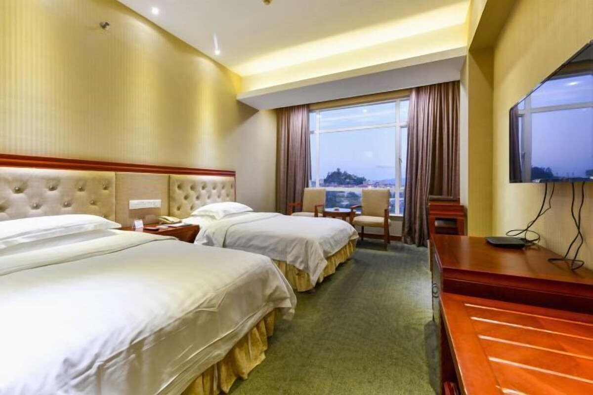 A hotel room with two beds, a desk, a chair, a TV, and a window with curtains.