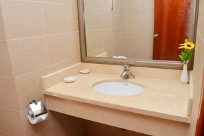 A bathroom with a beige sink, a mirror, and a toilet paper holder. - Wanghailou Hotel (Huizhou)